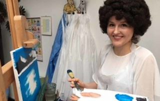 single lady with putty knife, palette and Bob Ross wig paints on a landscape