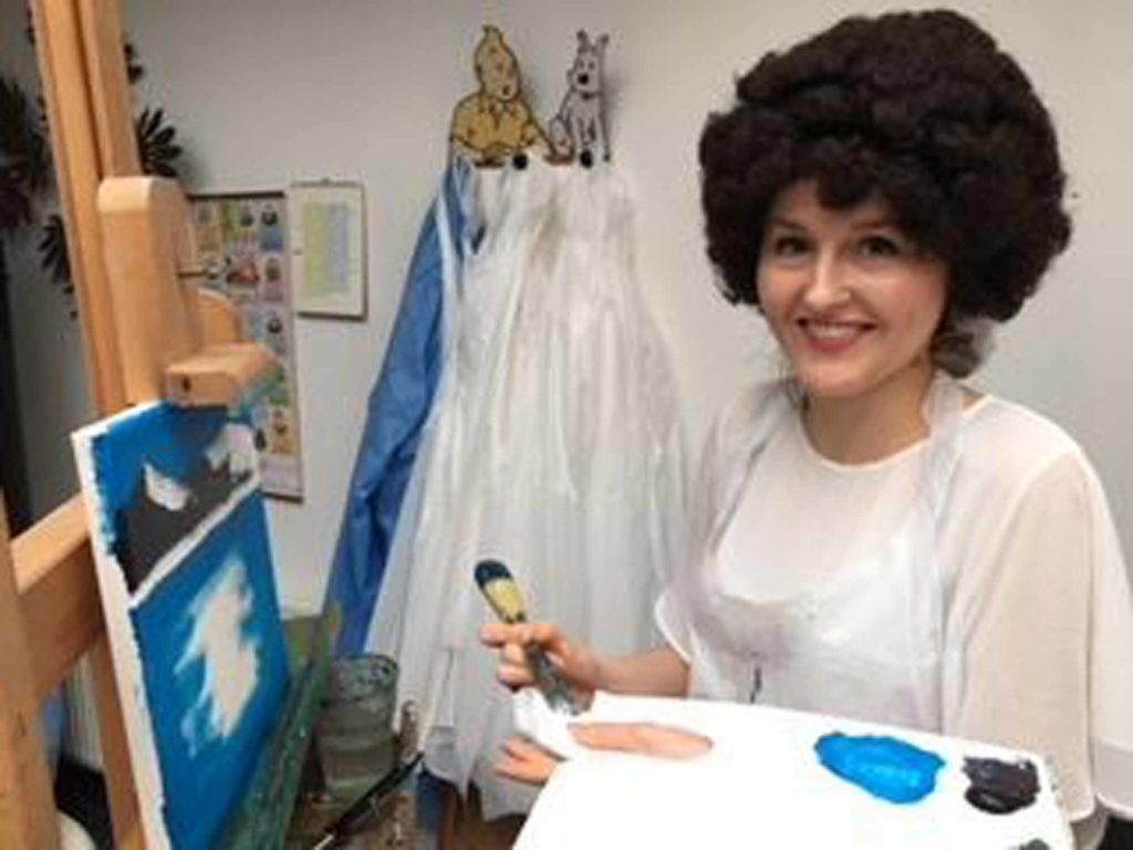single lady with putty knife, palette and Bob Ross wig paints on a landscape